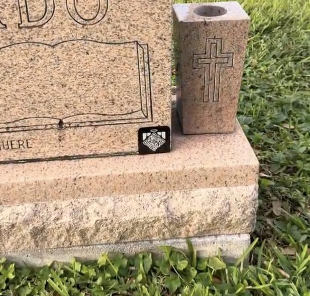 Memoriv medallion on a granite headstone base next to a cross